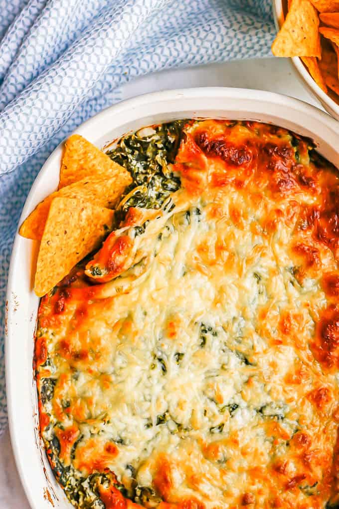 A browned and cheesy baked healthy spinach dip in a white casserole dish with tortilla chips tucked into the corner for dipping