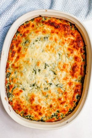 Browned, cheesy topped spinach dip in a white oval dish after baking