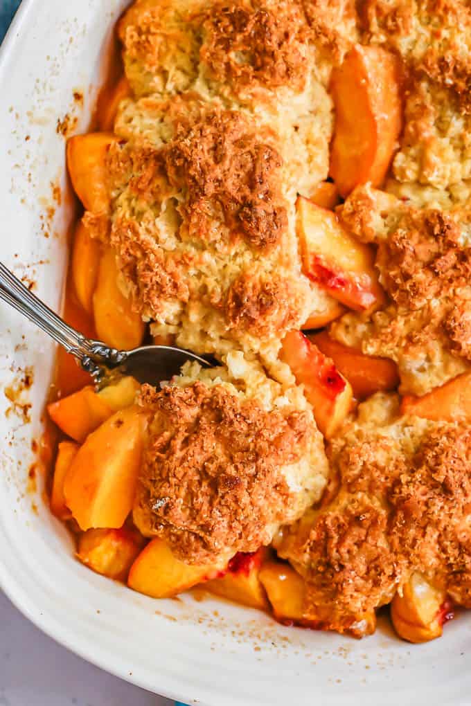 Close up of a spoonful of peach cobbler being taken from a casserole dish