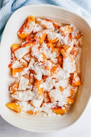 Sliced peaches in a white casserole dish with sugar and flour sprinkled on top