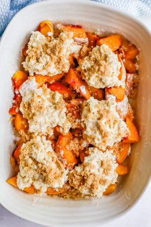 A white casserole dish with a peach cobbler being assembled before being baked