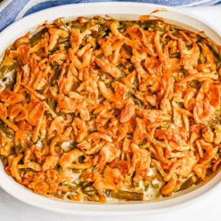 Green bean casserole with browned, crispy French fried onions on top in a white oval baking dish after cooking