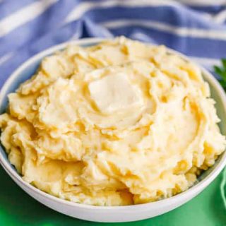 Creamy mashed potatoes with a pat of butter on top in a blue and white serving bowl with a sprig of parsley in the background