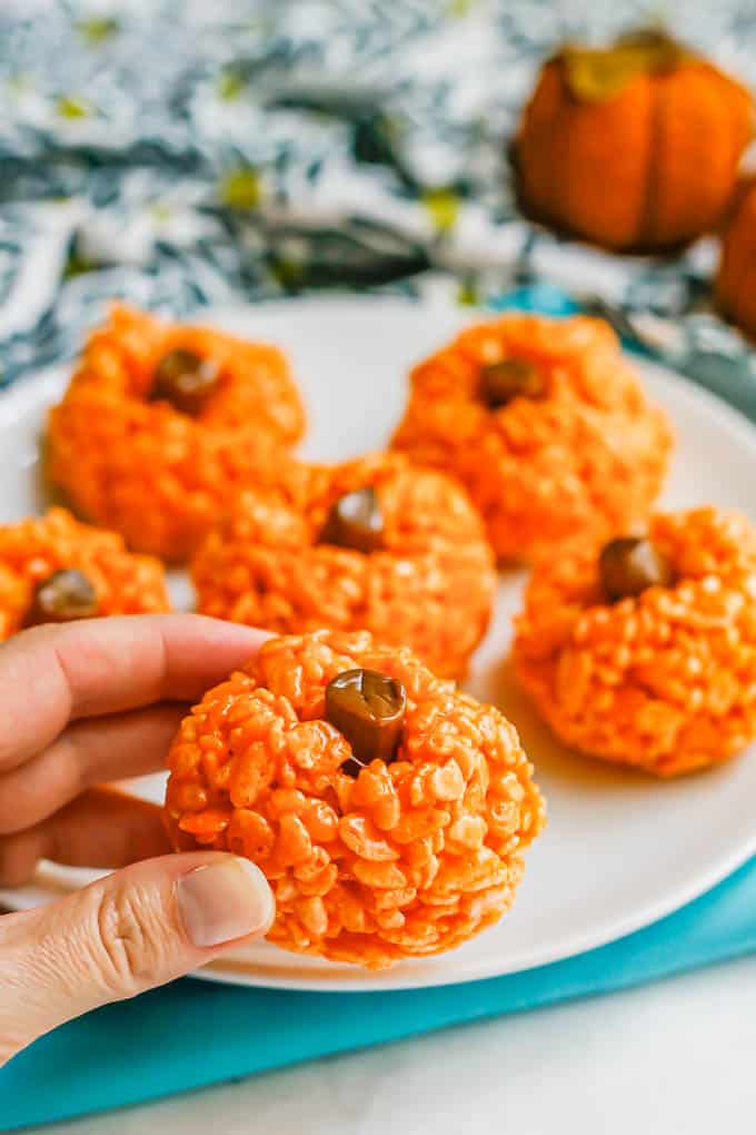 A hand picking up a pumpkin Rice Krispie treat from a plate