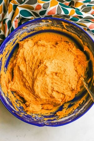 A big blue bowl with an orange cookie batter to make pumpkin cookies