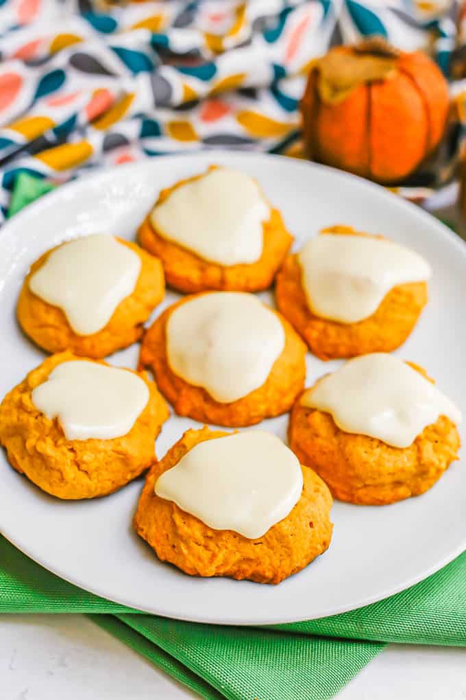 A white plate with 7 pumpkin cookies topped with a white icing, with green napkins underneath