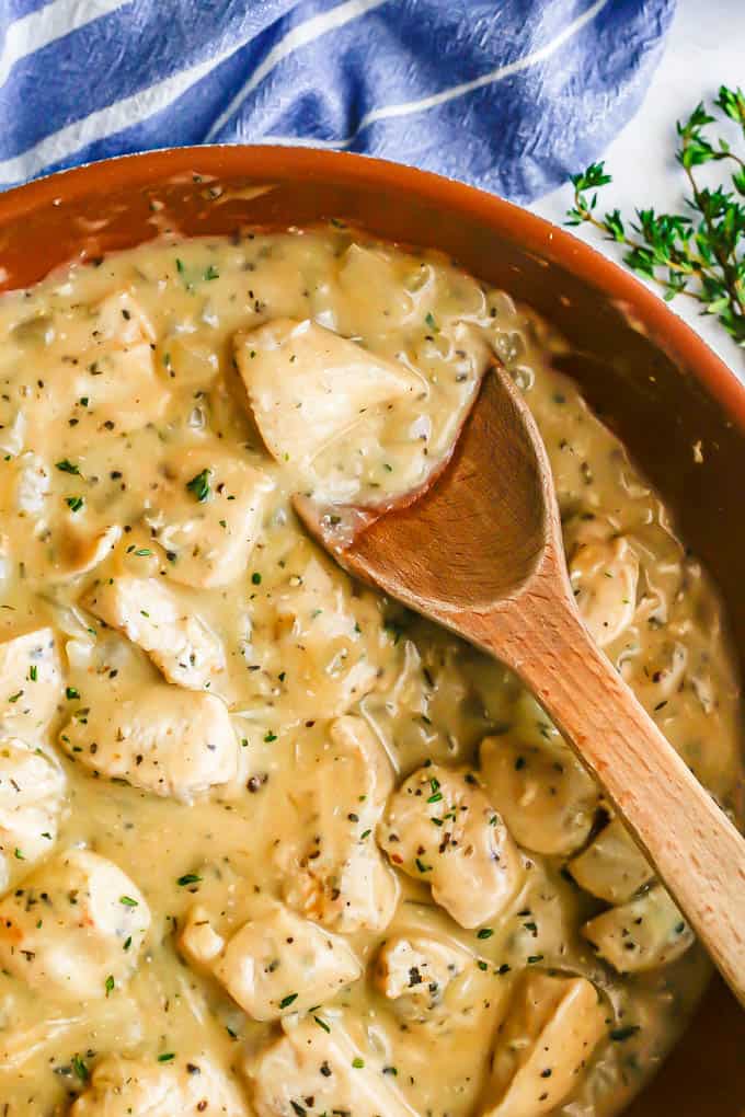 A copper skillet with cubed chicken in gravy with a wooden spoon resting in the skillet