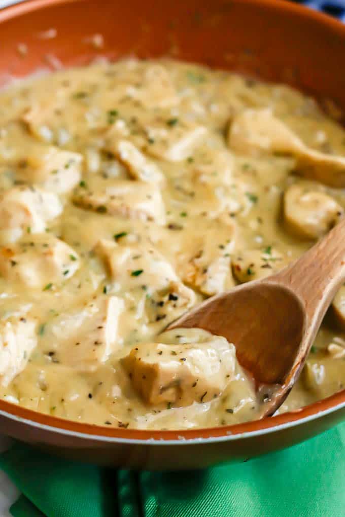 A wooden spoon resting in a copper skillet with creamy chicken and gravy