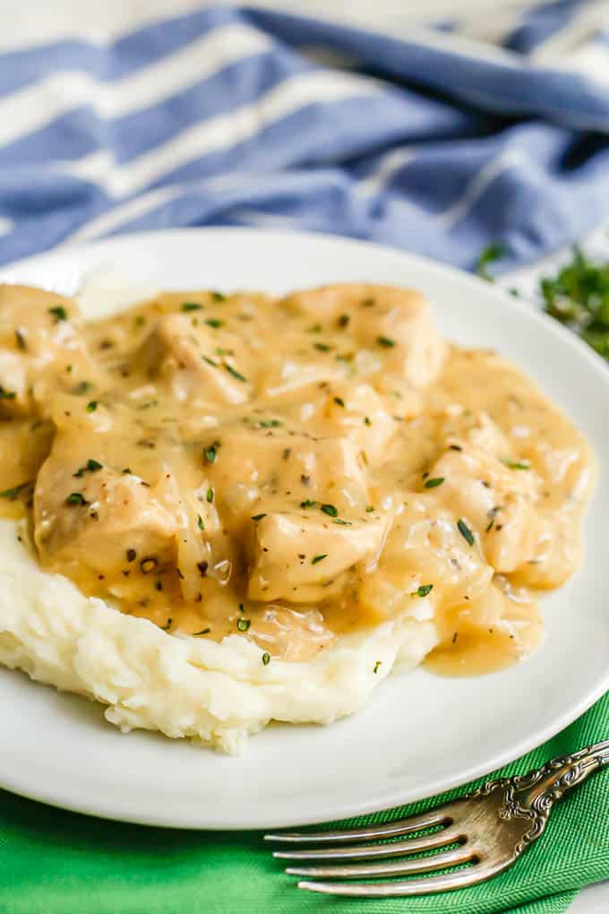 Close up of chicken and gravy over mashed potatoes on a white plate with a fork to the side