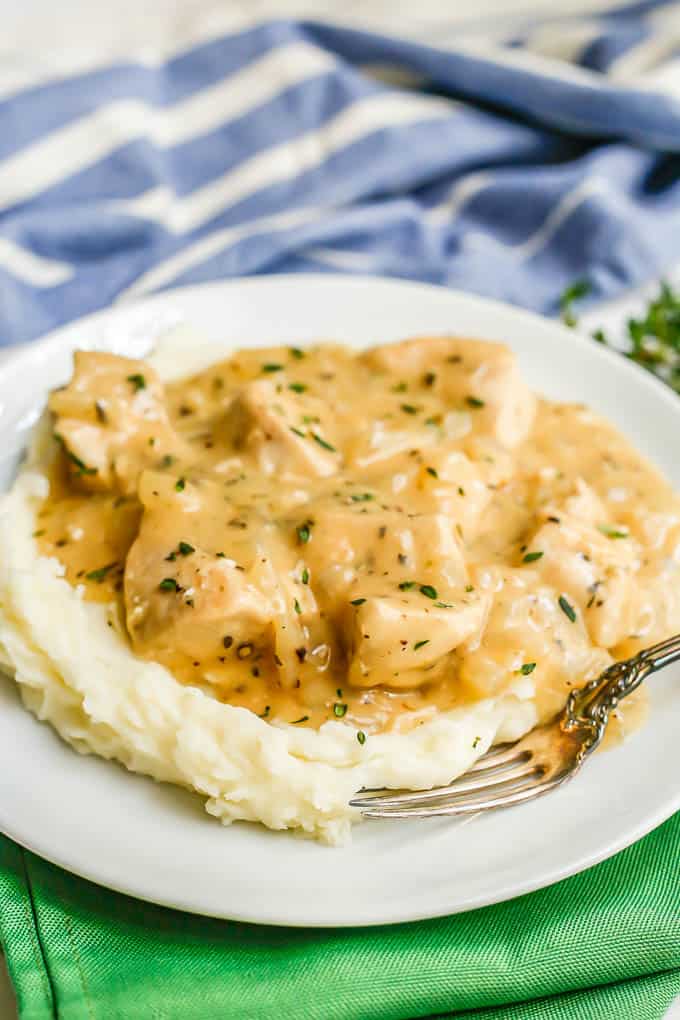 Chicken and gravy served over mashed potatoes on a white plate with a fork on the side