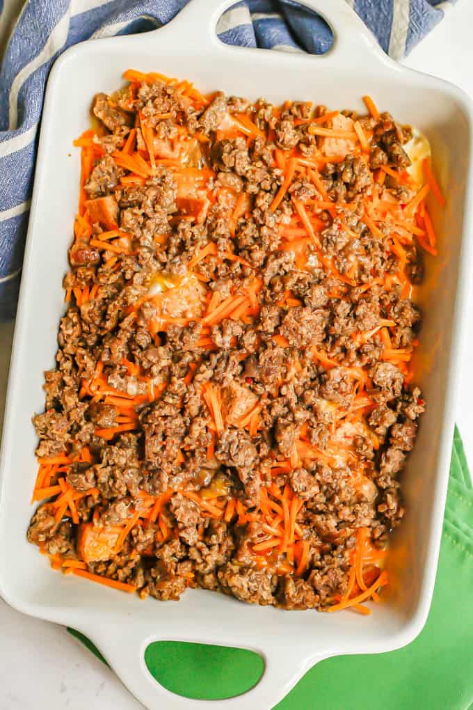 A breakfast casserole being assembled in a large white baking dish before being baked