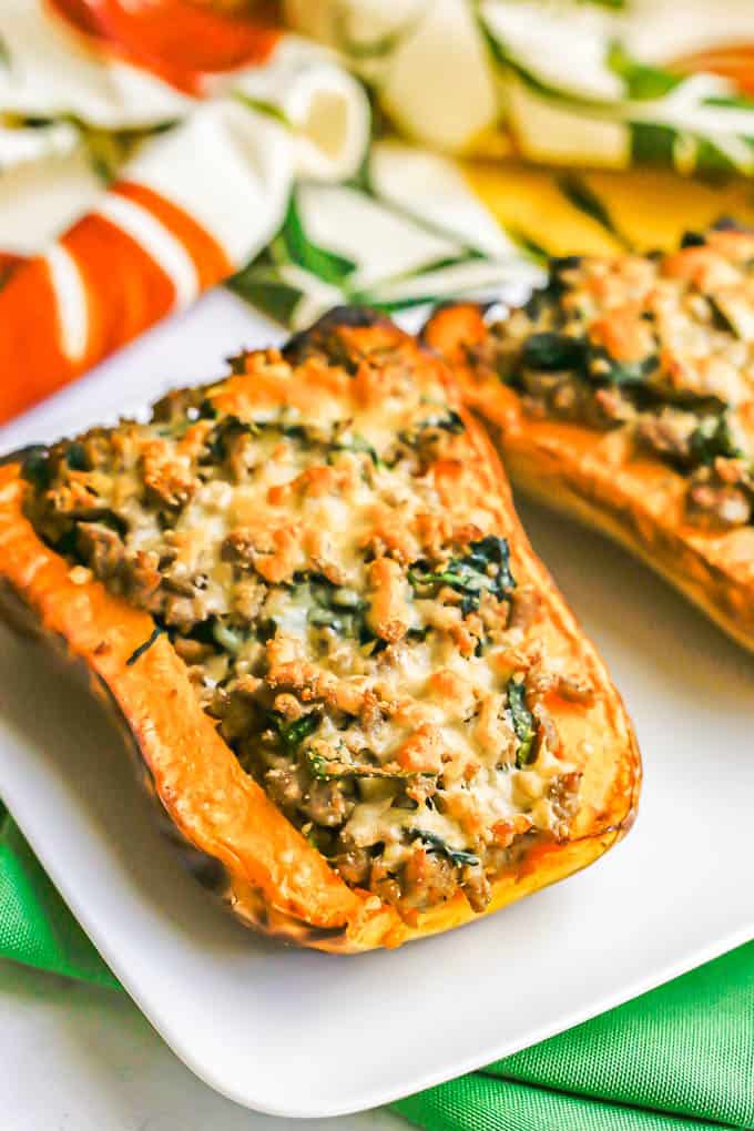 Angled side view of a butternut squash with sausage and spinach and browned Parmesan cheese on top