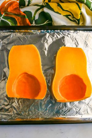 A halved butternut squash on a foil lined baking sheet before being roasted in the oven