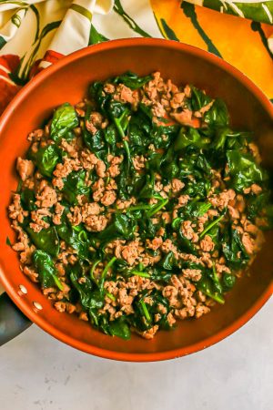 Cooked crumbled turkey sausage and wilted spinach in a copper skillet