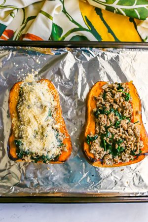 Sausage stuffed butternut squash with spinach and Parmesan cheese being prepped on a foil lined baking sheet before going in the oven