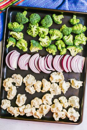 Broccoli, cauliflower and red onion slices on a sheet pan before being roasted in the oven