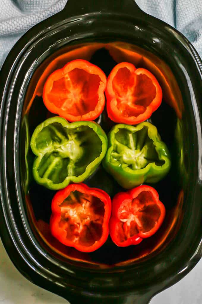 Six hollowed out bell peppers in a crock pot insert before being stuffed and cooked