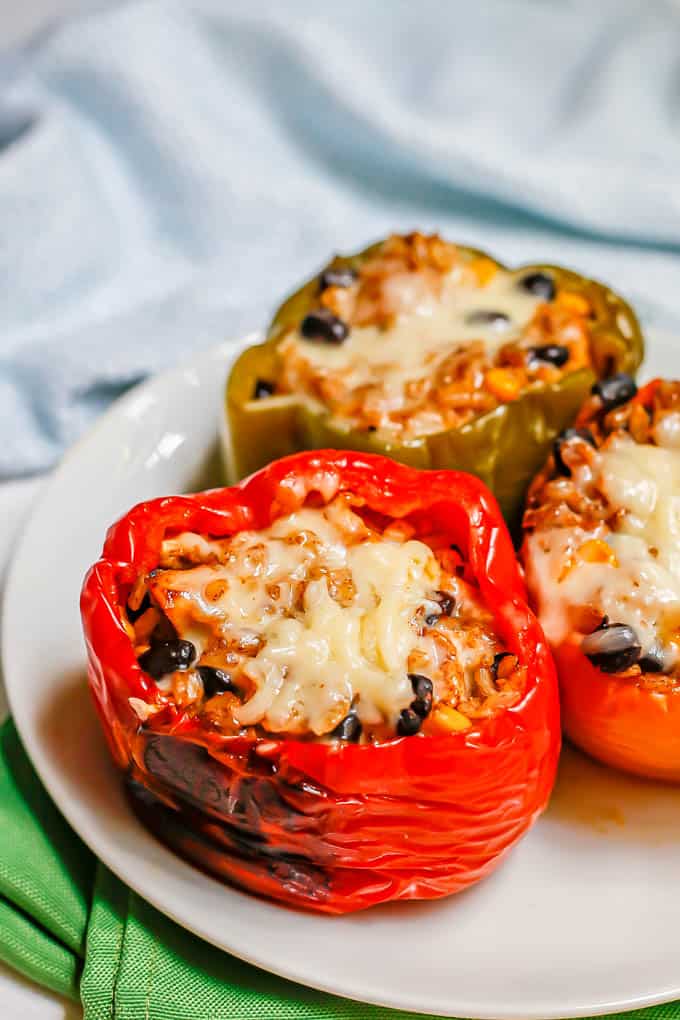 Three stuffed bell peppers on a white plate with melted cheese over the top