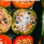 Six multi colored stuffed peppers in a slow cooker insert after being cooked with some melted cheese on one and a text overlay on the photo