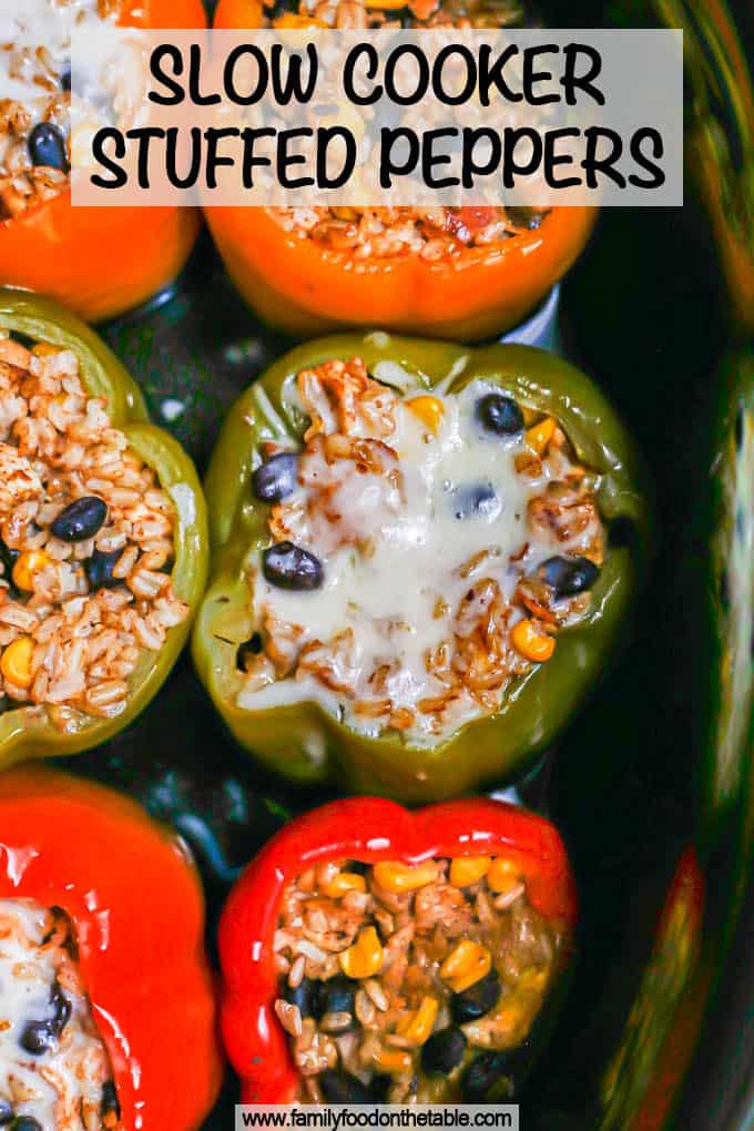 Six multi colored stuffed peppers in a slow cooker insert after being cooked with some melted cheese on one and a text overlay on the photo