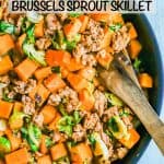A large skillet with turkey sausage, sweet potatoes and Brussels sprouts with a wooden spoon resting in the pan and a text overlay on the photo