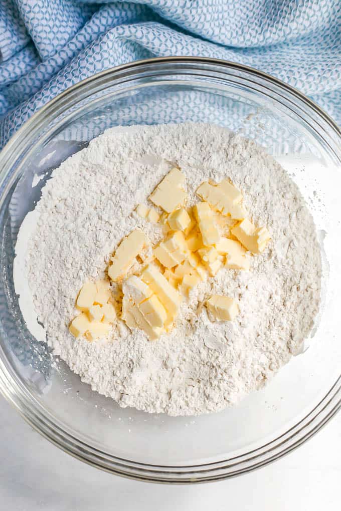 Small chunks of butter on top of a dry flour mixture in a glass bowl before being cut into the dough
