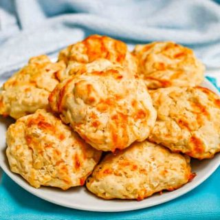A white serving plate of cheddar garlic drop biscuits set on a couple of turquoise napkins