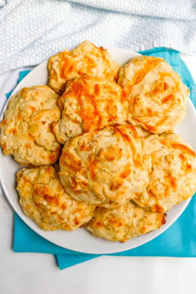 Overhead shot of cheddar drop biscuits stacked on a white plate set on turquoise napkins