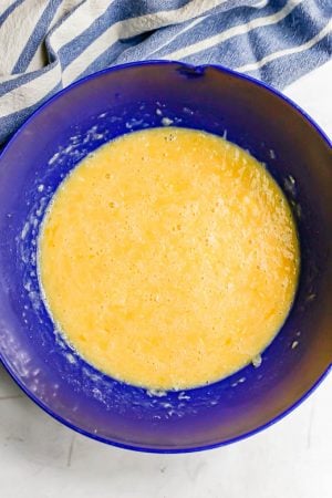 A large blue bowl with an egg and milk mixture in it and a blue striped towel in the background