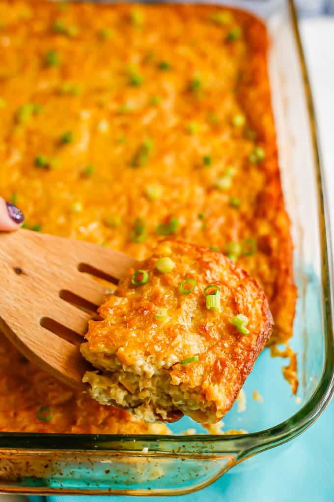 A square piece of corn pudding lifted up on a wooden spatula from the casserole dish