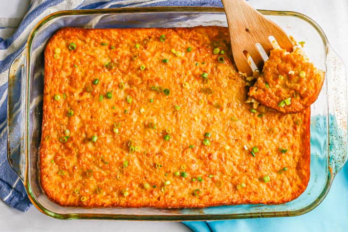 A wooden spatula picking up a square corner piece of corn pudding from a glass casserole dish