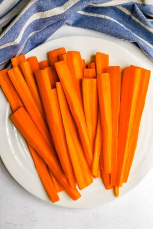 Cut strips of long, raw carrots on a white plate