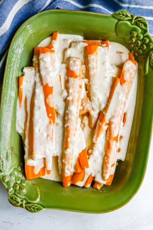 Carrots with a creamy white sauce in a green baking dish before being roasted