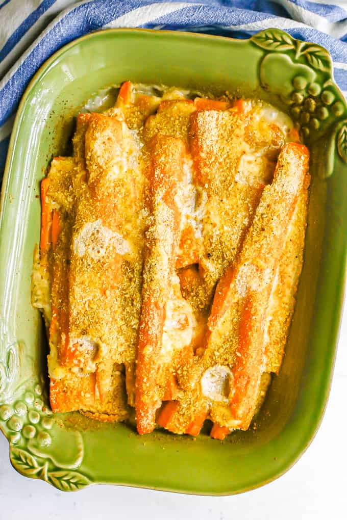 Carrots in a green baking dish with a creamy sauce coating the spears and buttery breadcrumbs on top after being baked