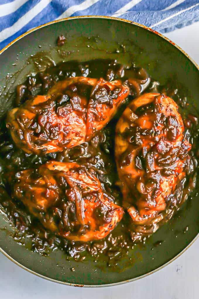 Chicken breasts in a pan with onions and a thick, reduced cranberry balsamic sauce