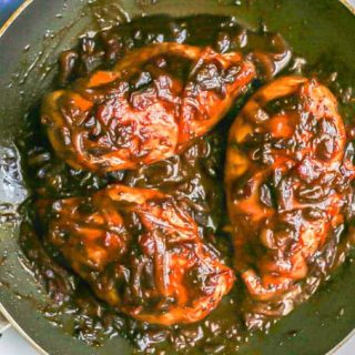 Three chicken breasts in a pan with onions and a thick, reduced cranberry balsamic sauce