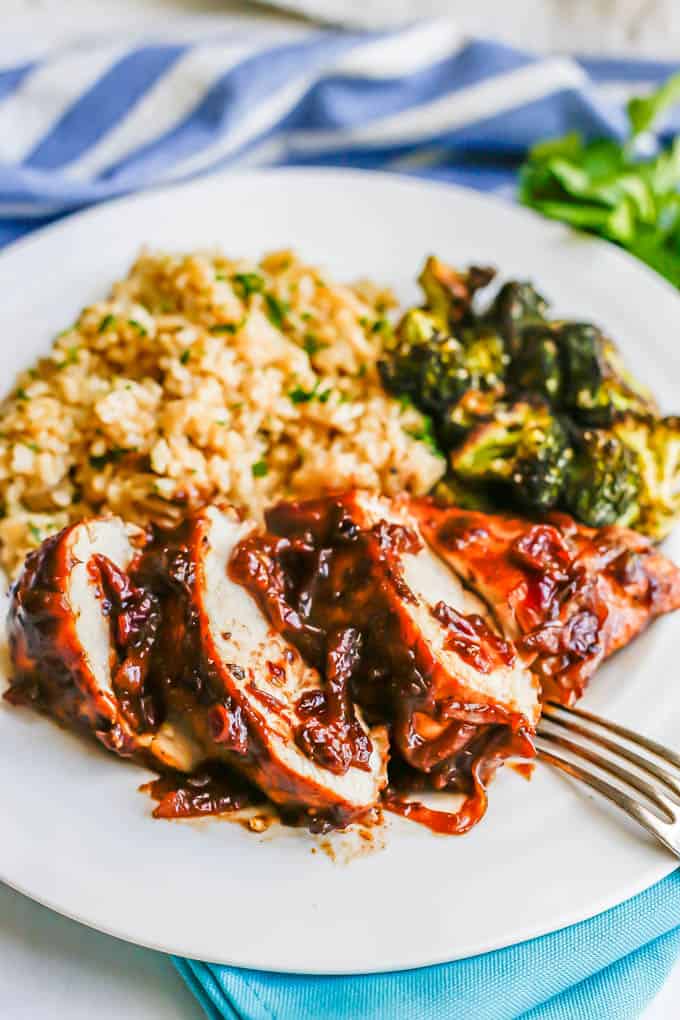 Sliced chicken breast with cranberry balsamic sauce on a white dinner plate with rice and broccoli