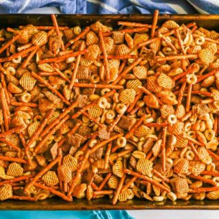 A baking pan full of homemade Chex mix with Chex, pretzels, peanuts and Cheerios after being cooked