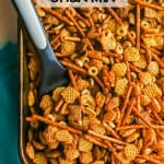 A spatula tucked into a baking pan full of homemade Chex mix with a text overlay on the photo