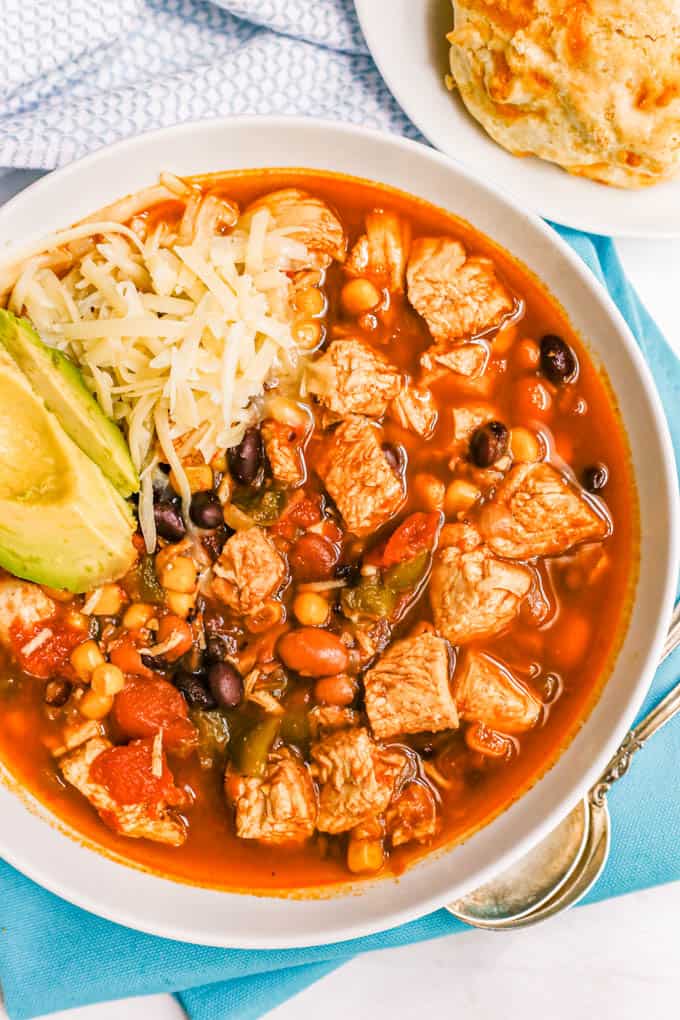 Close up of a white bowl with chunky chicken chili topped with cheese and avocado