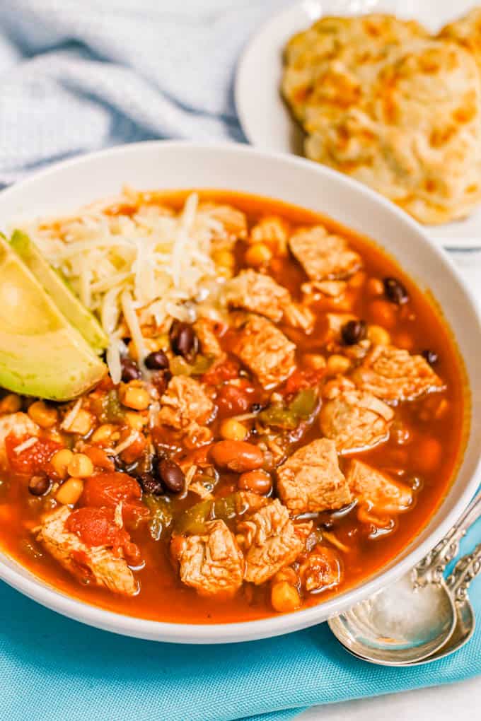 A bowl of chicken chili with black beans, pinto beans, corn and tomatoes with two spoons alongside the bowl