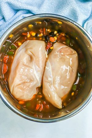 Two raw chicken breasts on top of a chili mixture of beans, corn and tomatoes in an Instant Pot before being cooked