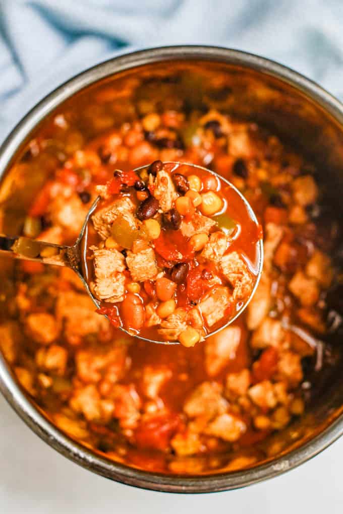 A silver ladle holding up a scoop of chicken chili from the insert of an Instant Pot