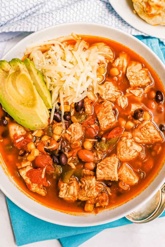 A large white bowl with chicken chili topped with shredded cheese and avocado