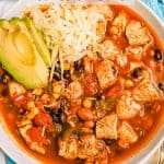 A large white bowl with chicken chili topped with shredded cheese and avocado and a text overlay on the photo
