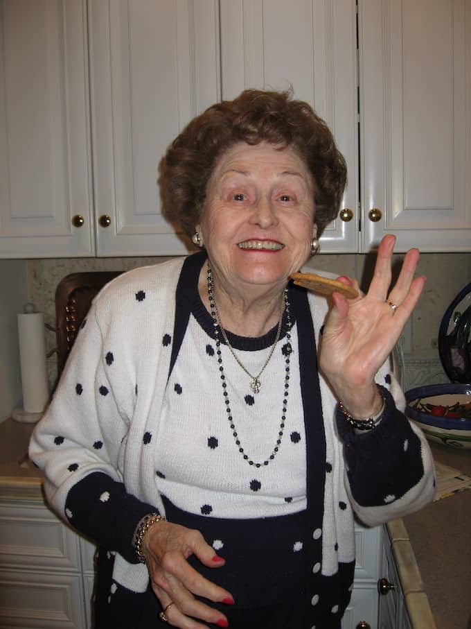 A grandmother holding a chocolate chip cookie with a big smile on her face