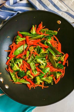 A mix of broccoli, snow peas, carrots and red pepper being cooked in a large wok