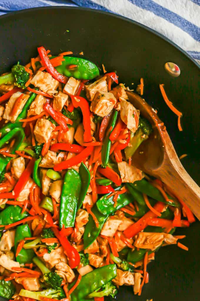 A wooden spoon tucked into a wok full of a diced turkey and vegetable stir fry