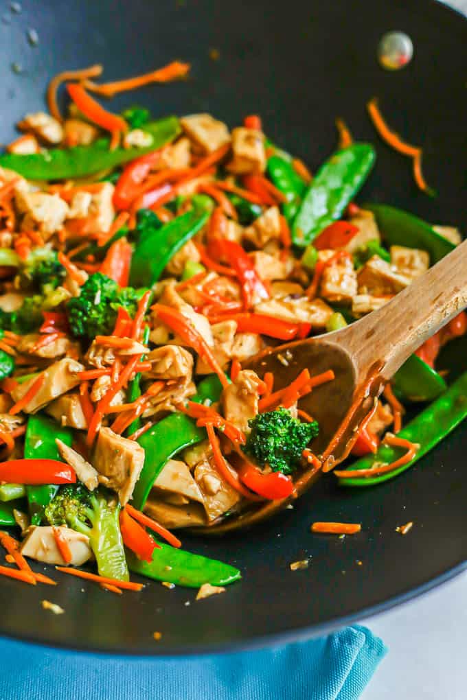A dark wok with leftover turkey stir fry with colorful veggies and a wooden spoon scooping up the mixture
