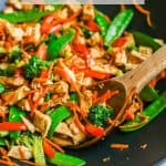 A dark wok with leftover turkey stir fry with colorful veggies and a wooden spoon scooping up the mixture and a text overlay on the photo